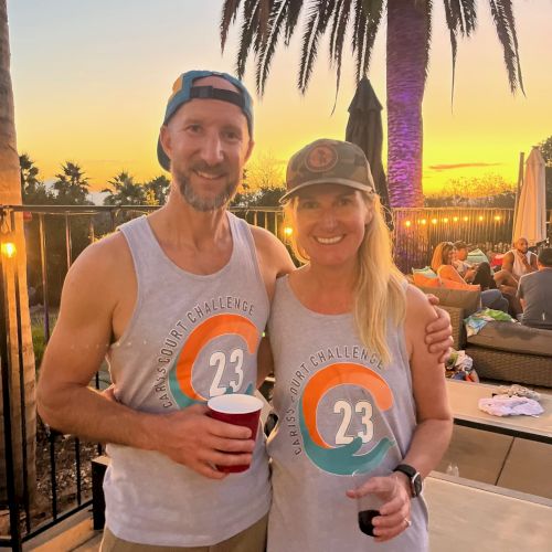Two people wearing matching tank tops with the number 23, standing together outdoors at sunset, palm tree in the background.