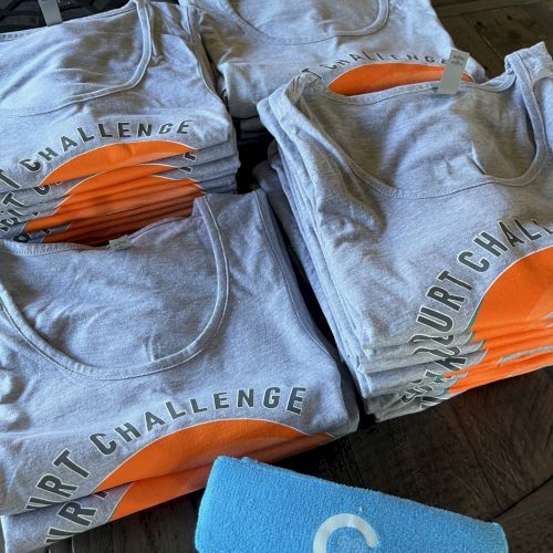The image shows stacks of folded t-shirts with a logo that reads 